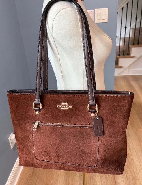 A brown suede Coach tote hanging on a dress form