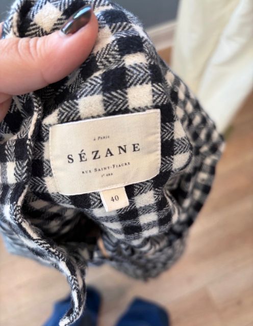A hand holding open a black and white checked coat to show its Sezane label