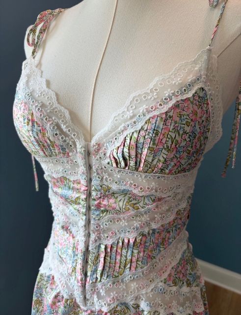A floral dress with white eyelet lace panels, close up on a dress form