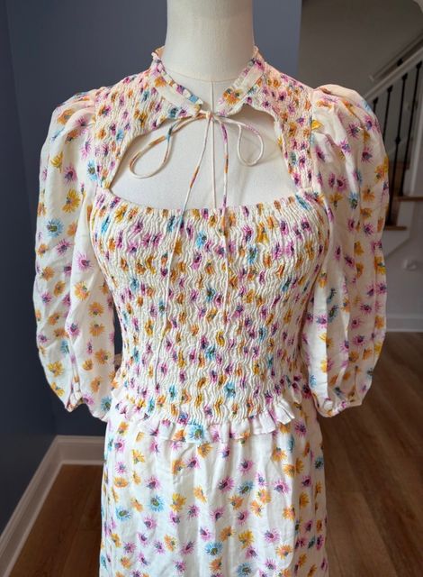 A cream floral smocked dress with puff sleeves on a dress form