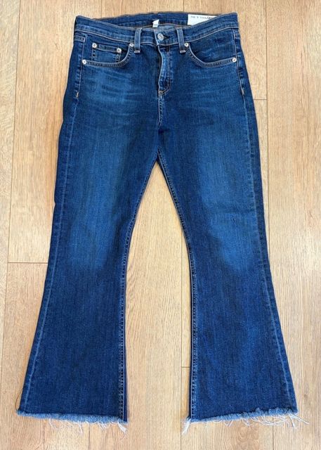Dark wash flared jeans with a raw hem, laid flat on a wood floor