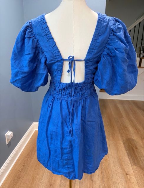 A cobalt blue linen romper with puff sleeves on a dress form, seen from the back