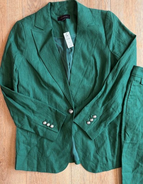 A green linen blazer and matching trousers laid flat on a wood floor